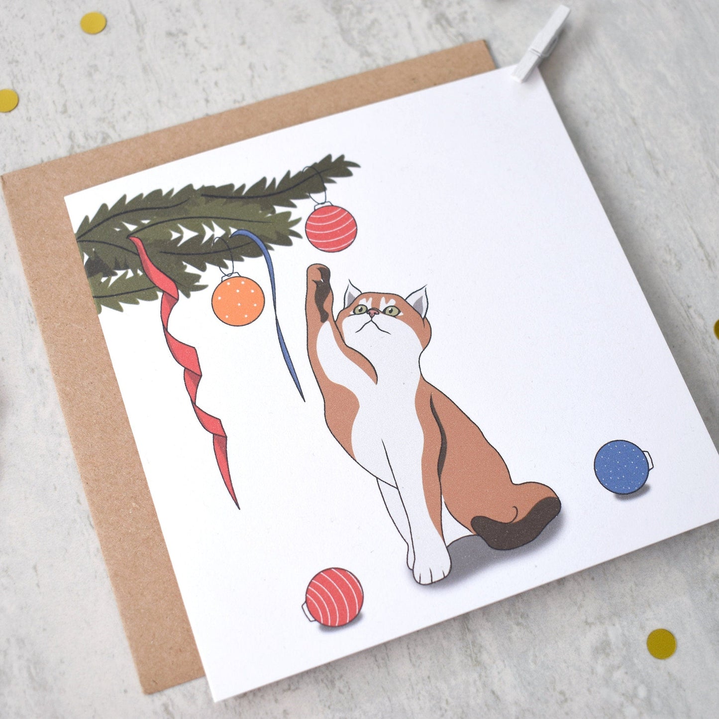 Greeting card with a cat playing with Christmas ornaments on a textured surface.