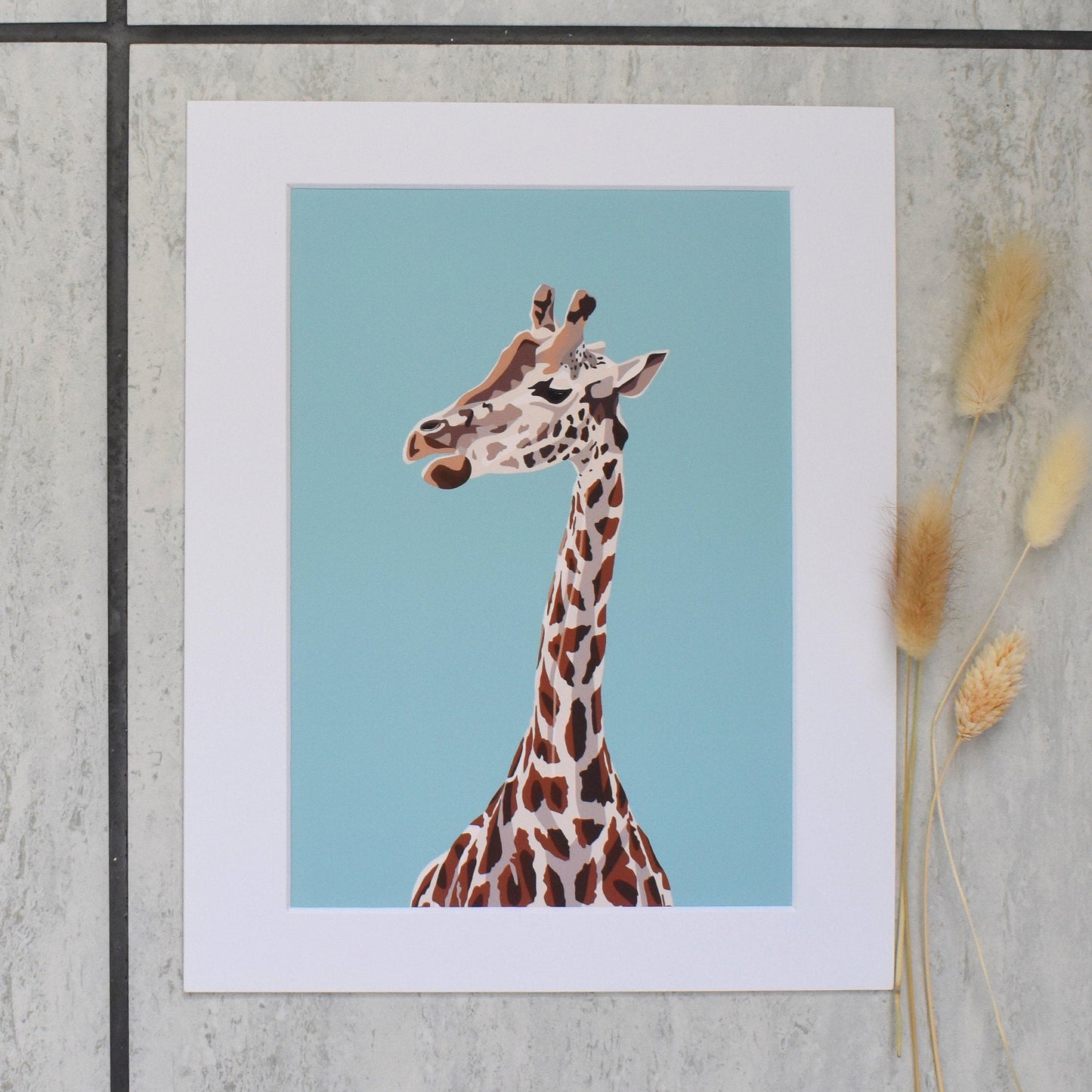 Framed artwork of a giraffe against a blue background on a textured wall.