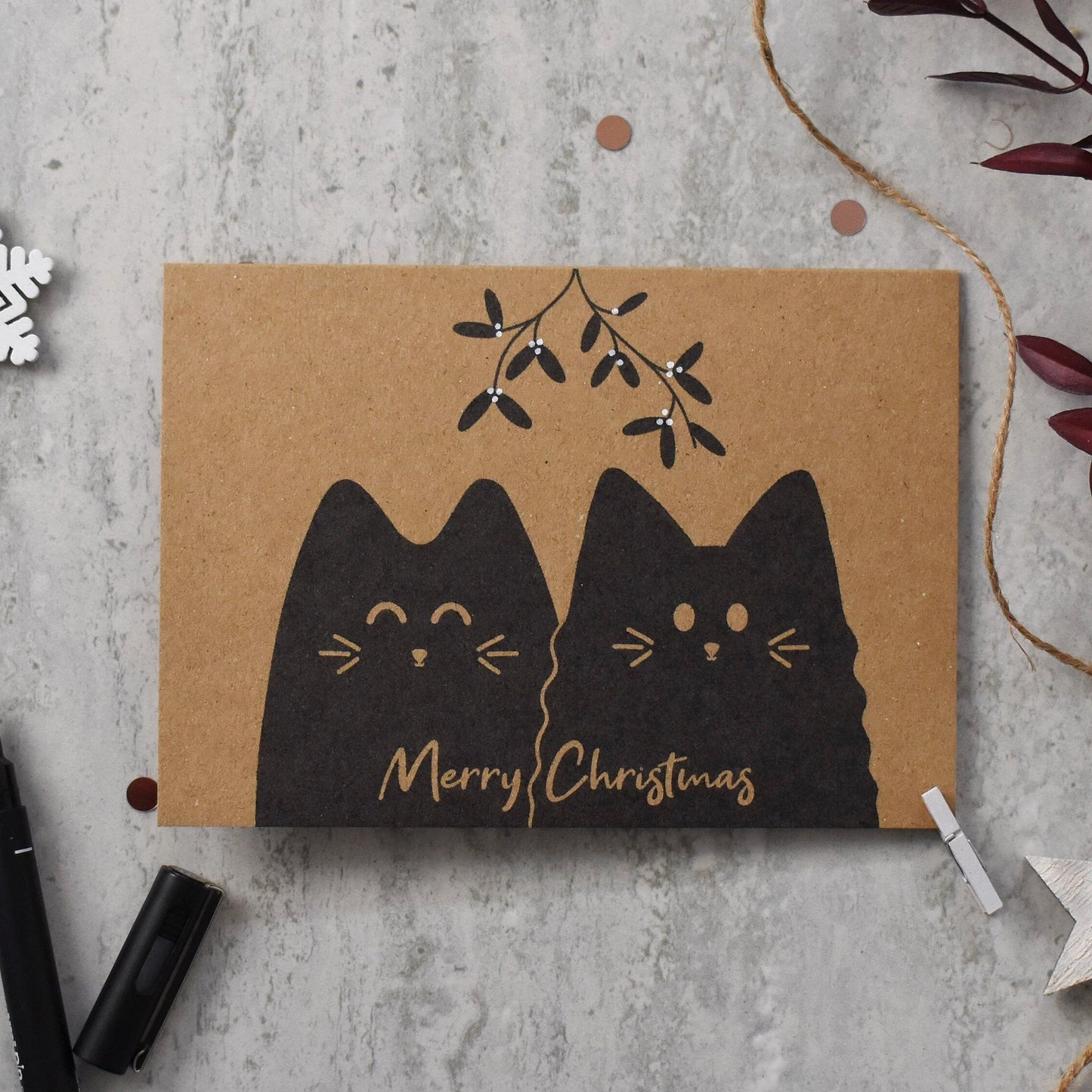 Card with black cats and 'Merry Christmas' text on a textured surface with decorative elements.