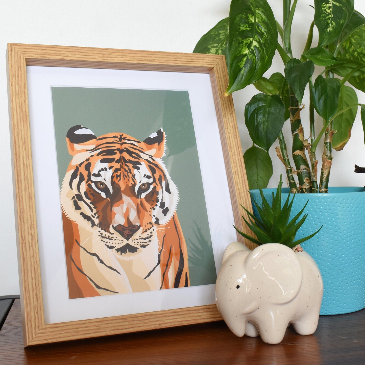 Framed artwork of a tiger, potted plant, and decorative items on a surface.
