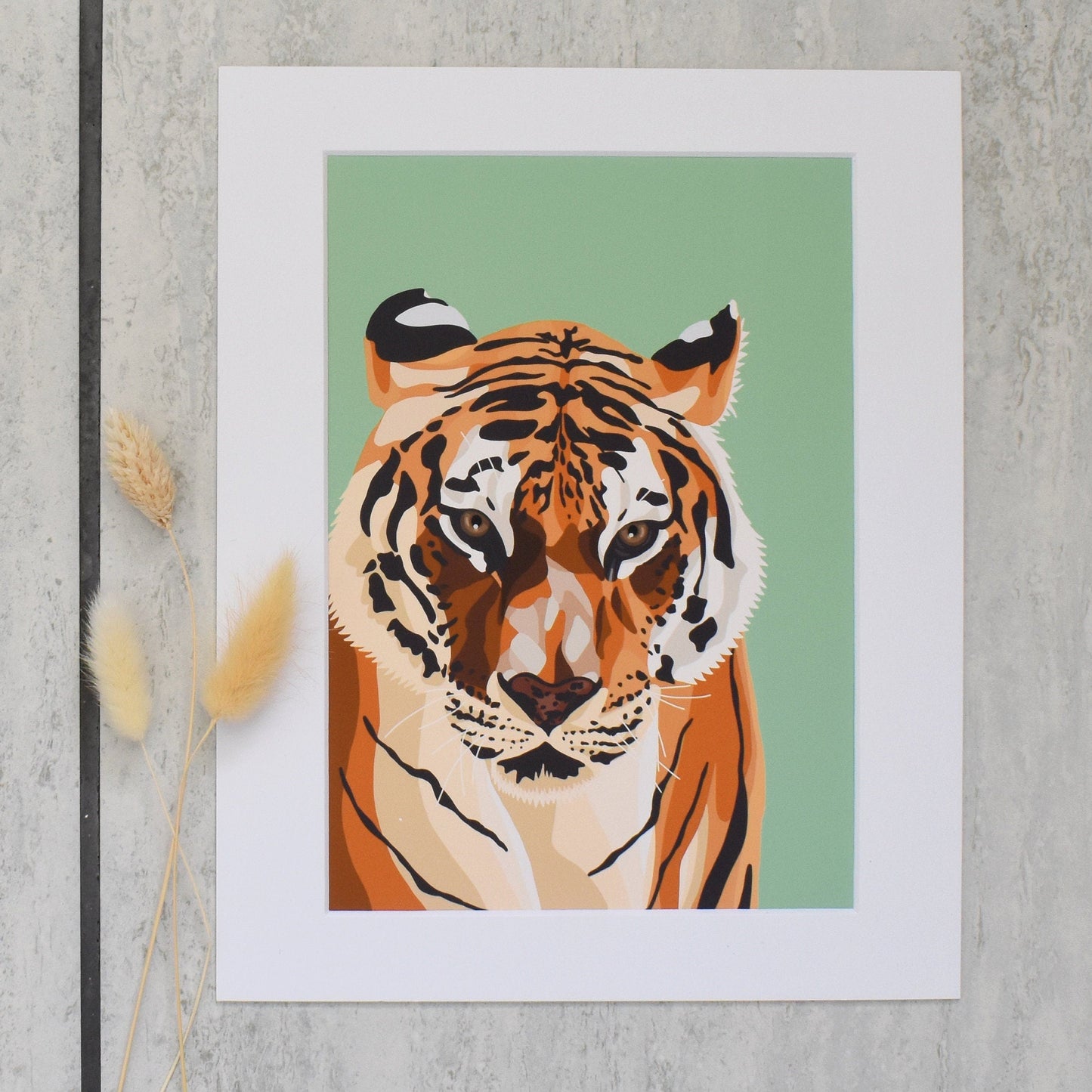 Framed artwork of a tiger on a green background, leaning against a textured wall.