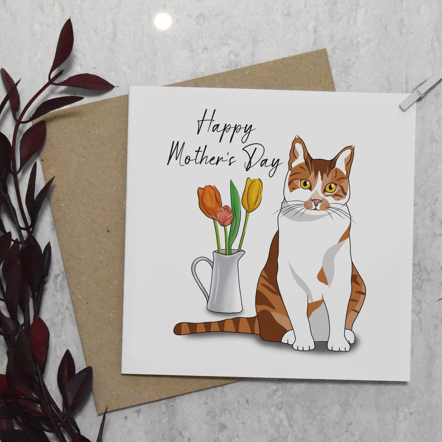 Mother's Day card with a cat illustration and flowers, placed on a textured surface.