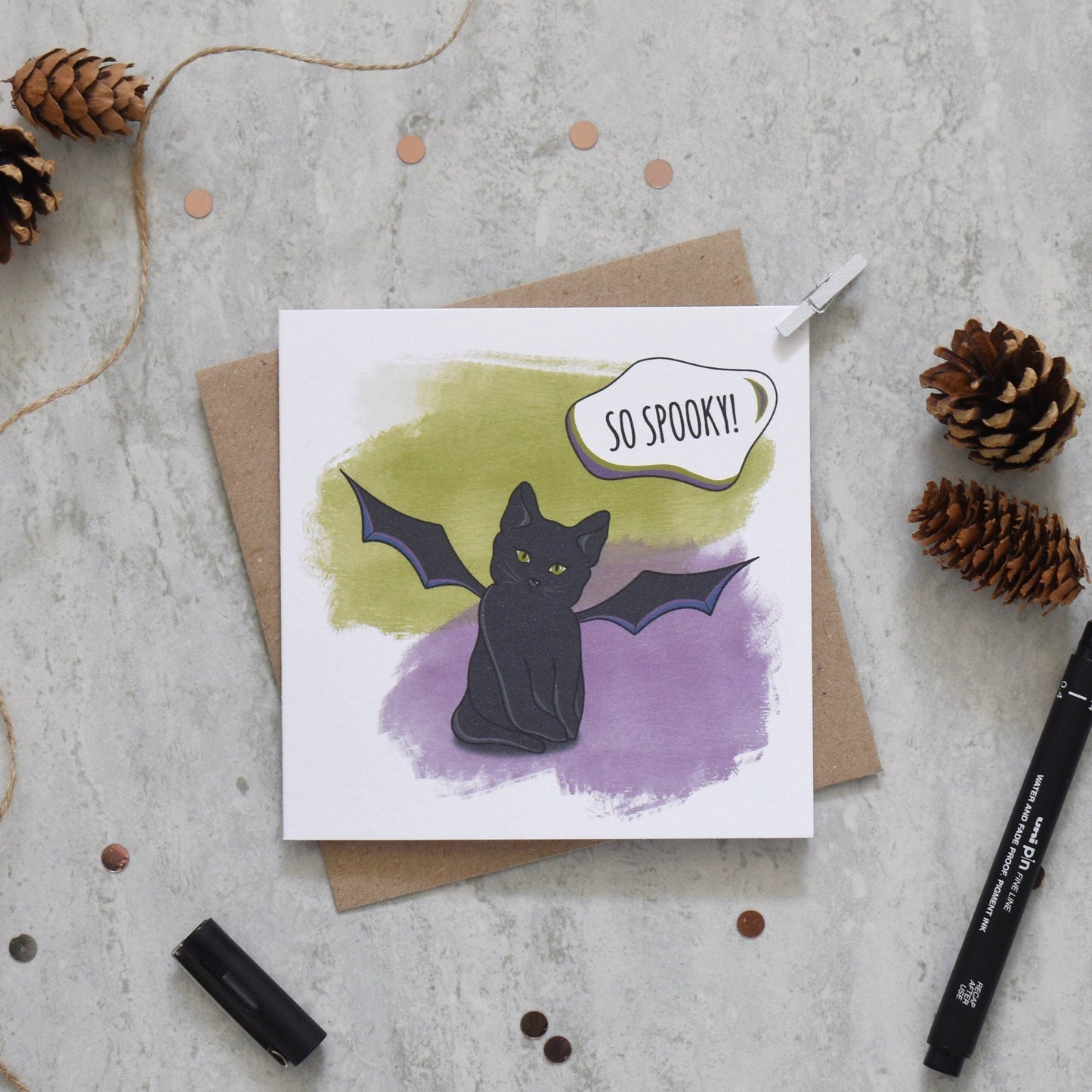 Greeting card with a black cat illustration and 'So Spooky!' text, surrounded by decorative items on a textured surface.