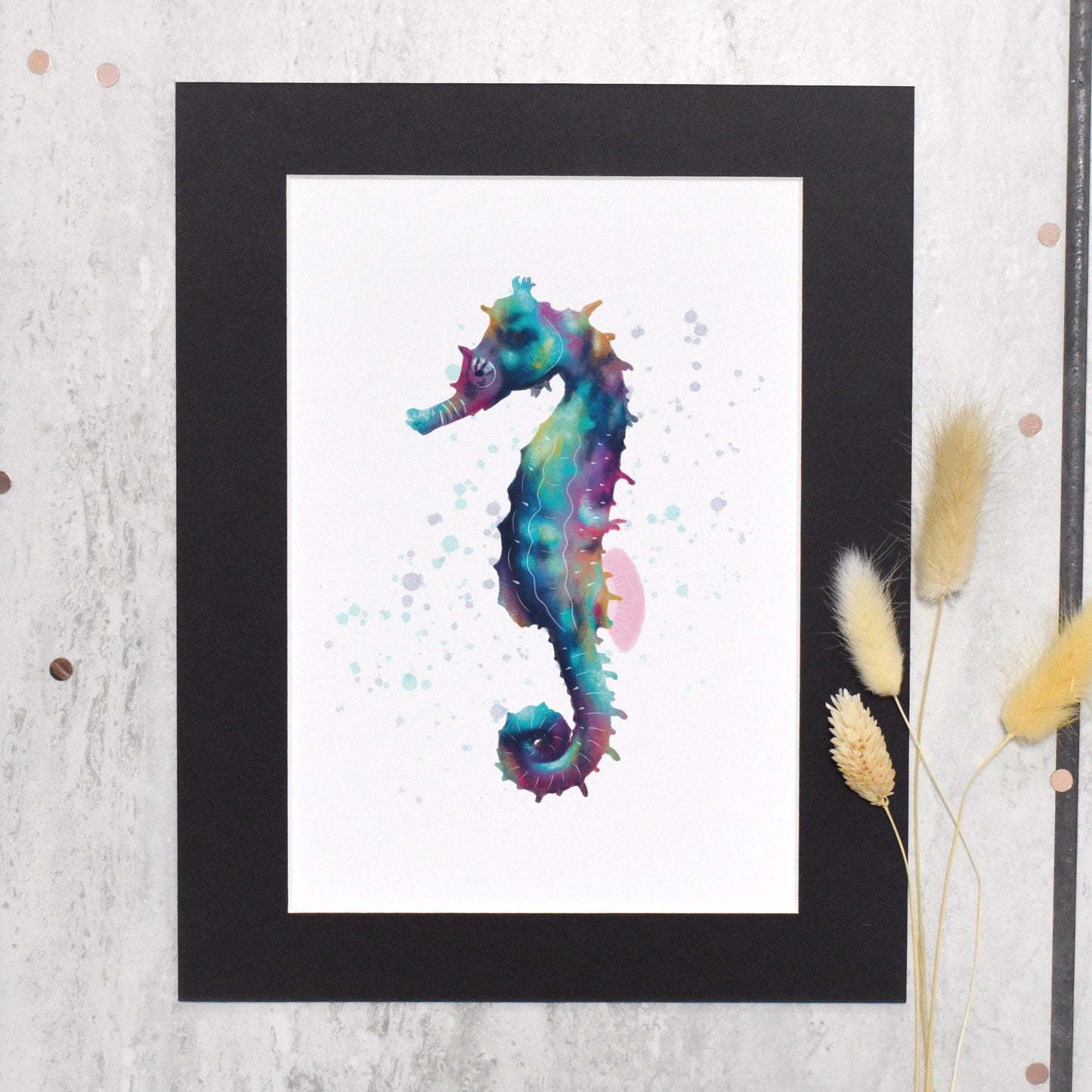 Framed watercolor painting of a seahorse on a textured wall with dried grasses.
