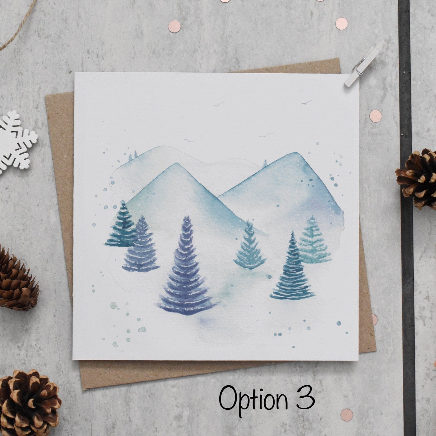 Card with watercolor mountains and trees on a textured surface with decorative elements.