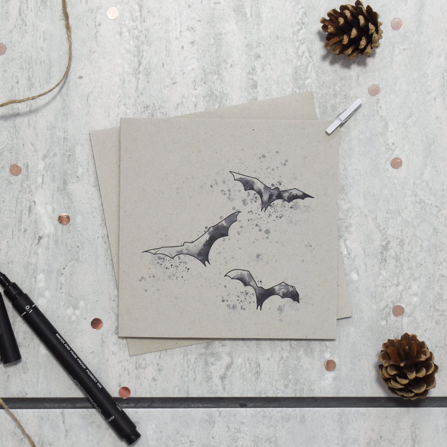 Card with bat illustrations on a textured surface with pine cones and a pen.