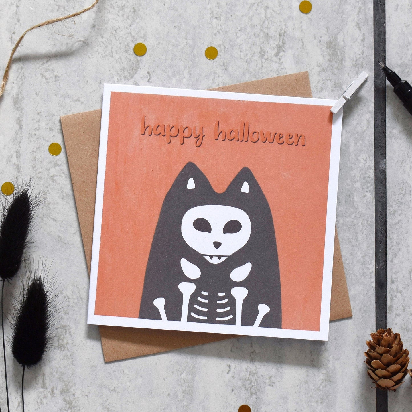 Halloween card with skeleton cat design on a textured surface with decorative elements.