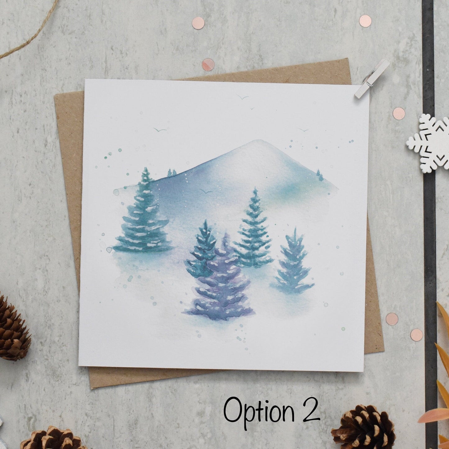 Winter-themed greeting card with trees and mountains, surrounded by decorative elements on a textured surface.
