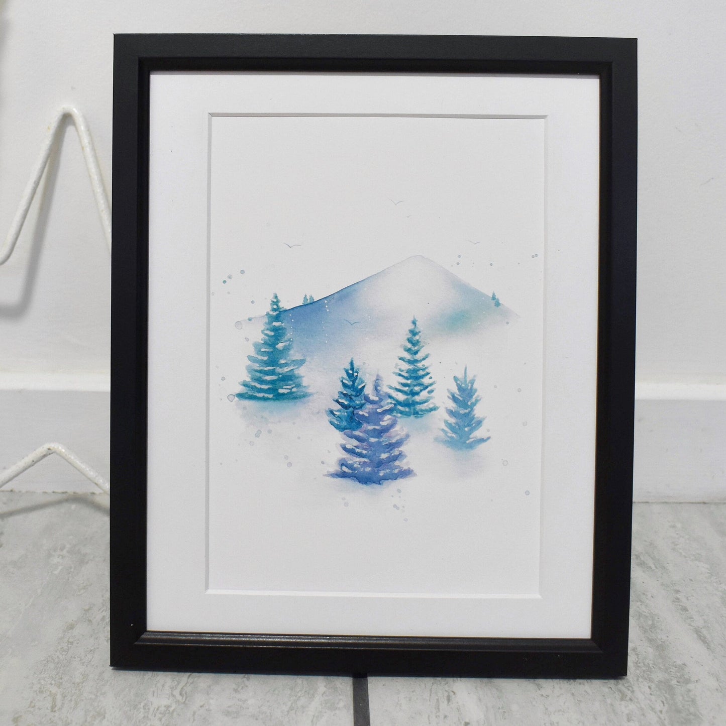 Framed artwork of blue trees and mountains on a white background