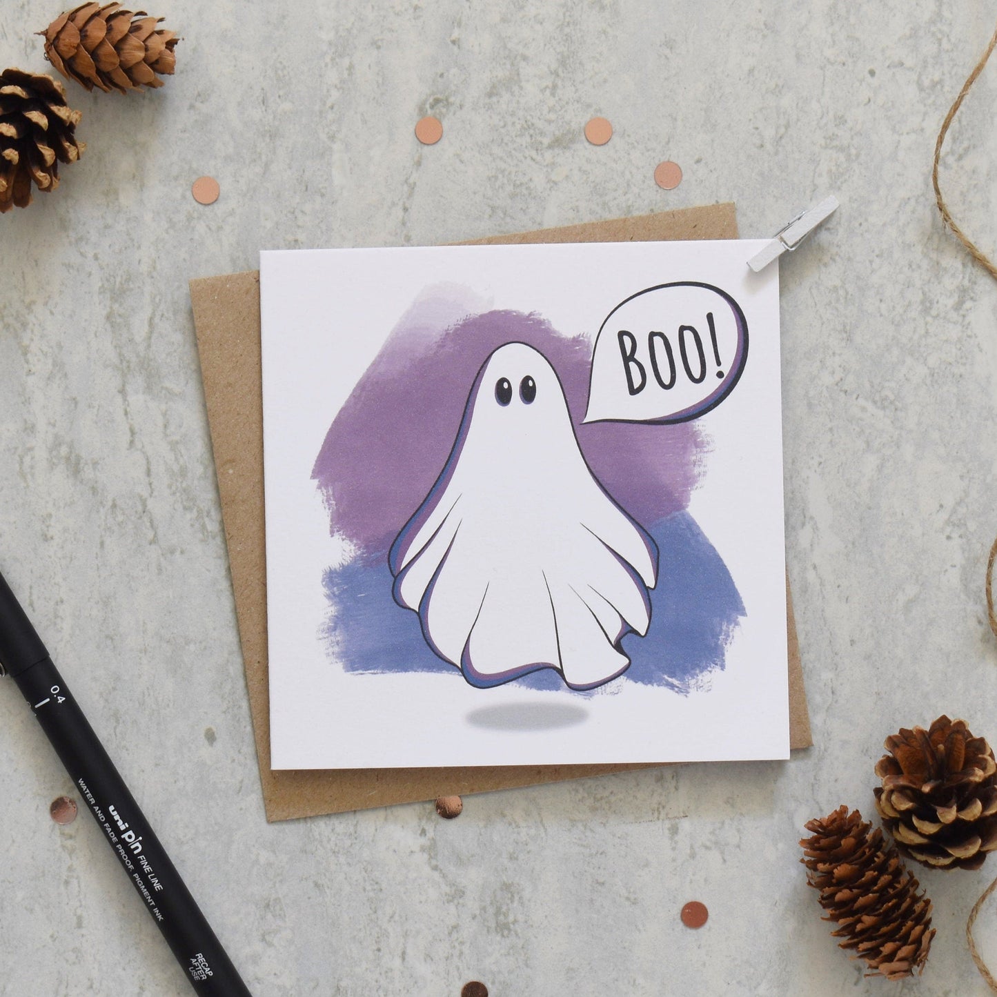 Greeting card with a ghost illustration and 'BOO!' text on a textured surface with decorative elements.