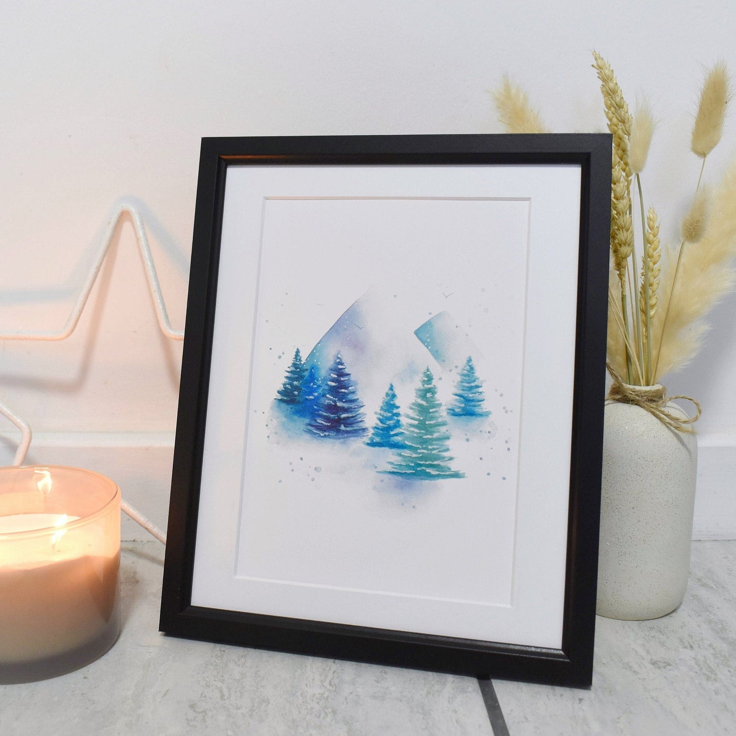 Framed artwork of trees with a candle and decorative elements on a light surface.