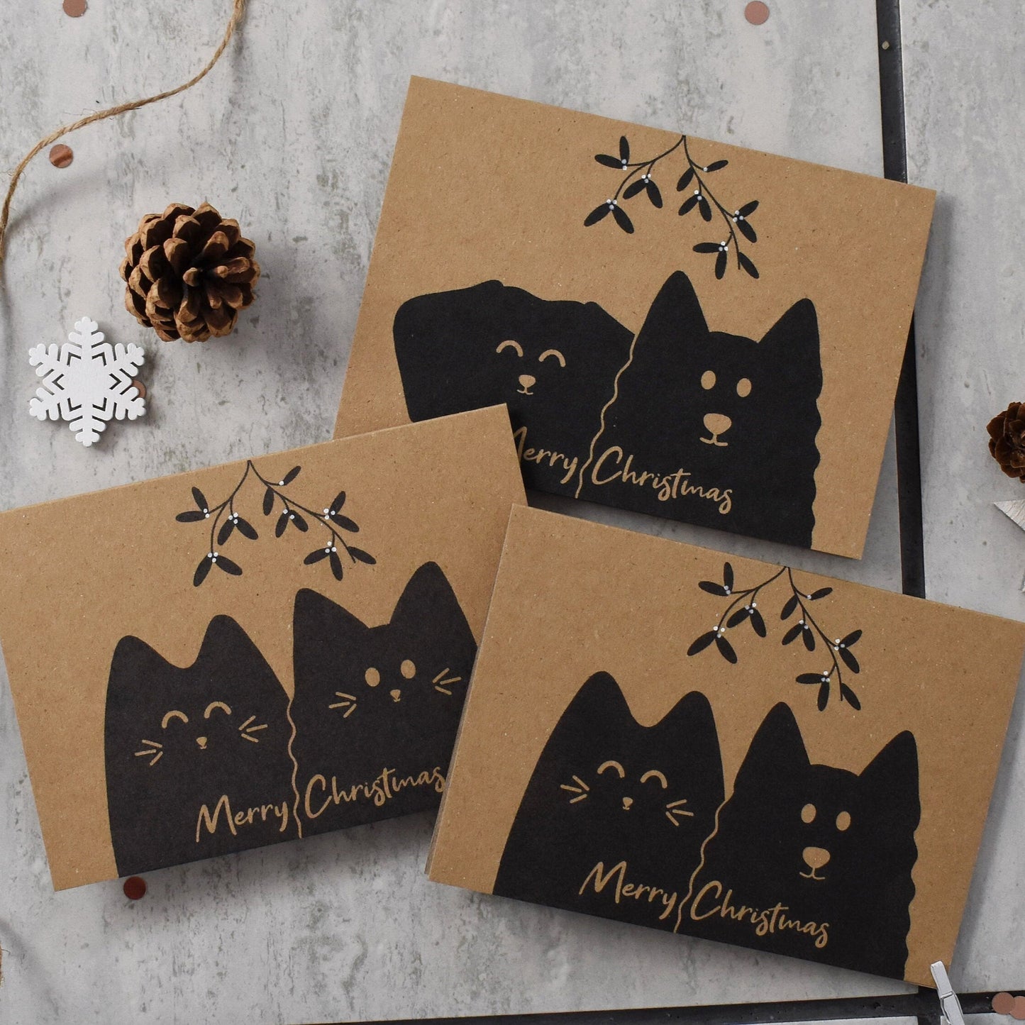 Three brown Christmas cards with black cat illustrations and 'Merry Christmas' text on a gray surface.