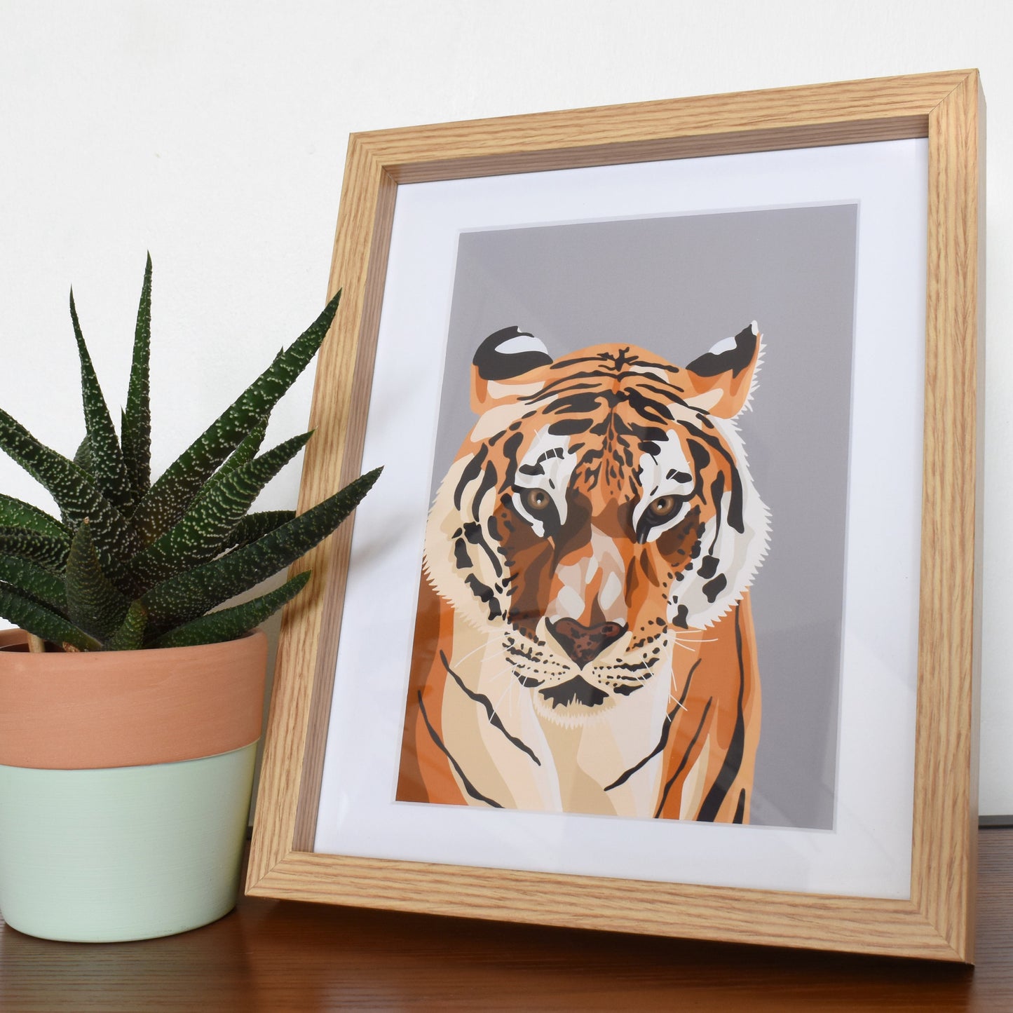 Framed artwork of a tiger next to a potted plant on a table.