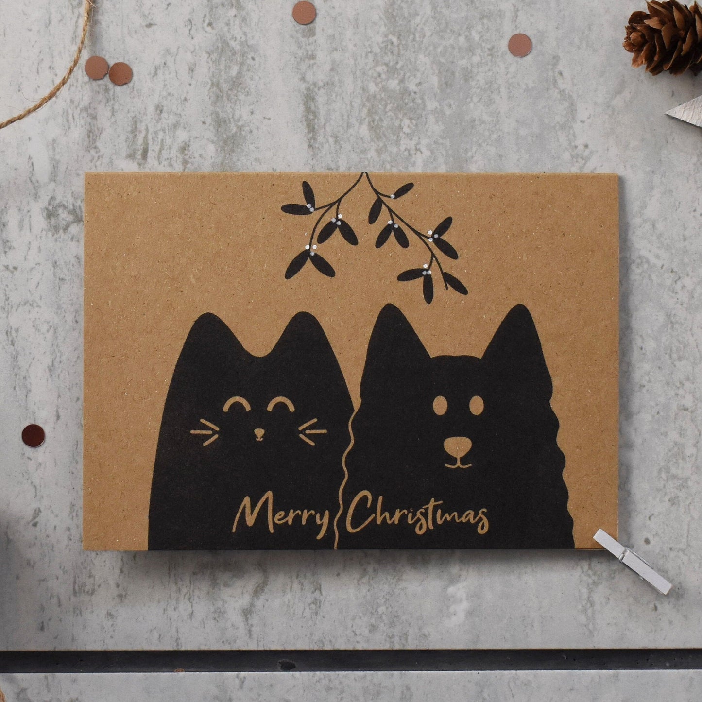 Kraft paper card with black cat illustrations and 'Merry Christmas' text on a gray surface with decorative elements.
