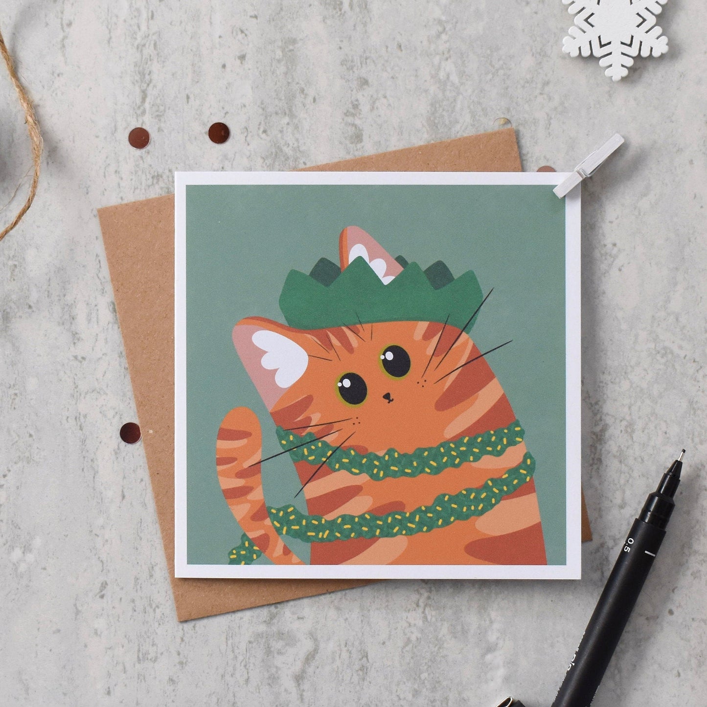 Card with a cat illustration wearing a green hat and scarf on a textured surface.