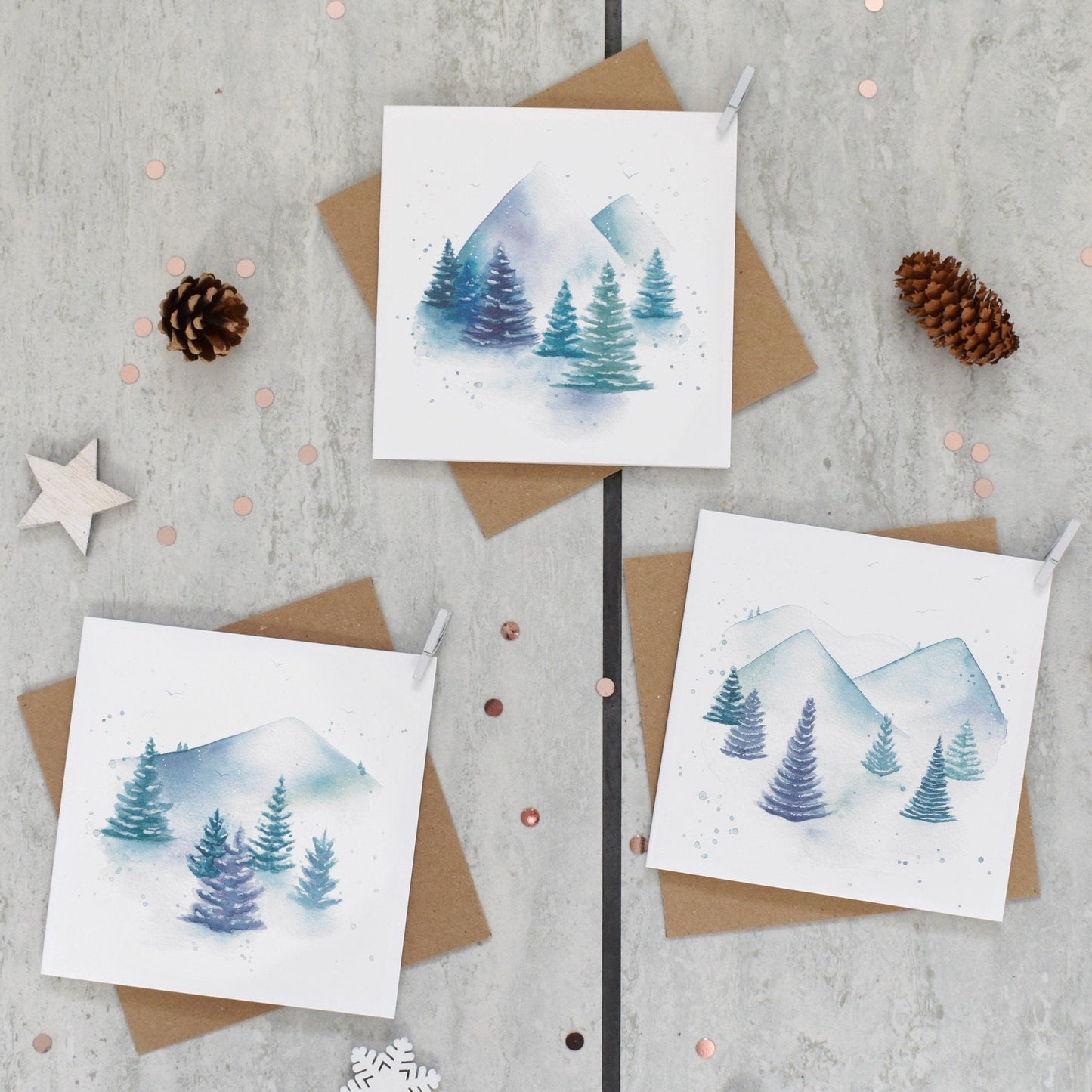 Three greeting cards with mountain and tree designs on a textured surface with decorative elements.