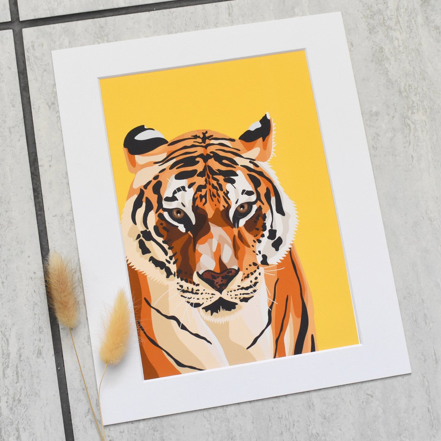 Art print of a tiger on a yellow background with a white border, placed on a textured surface.