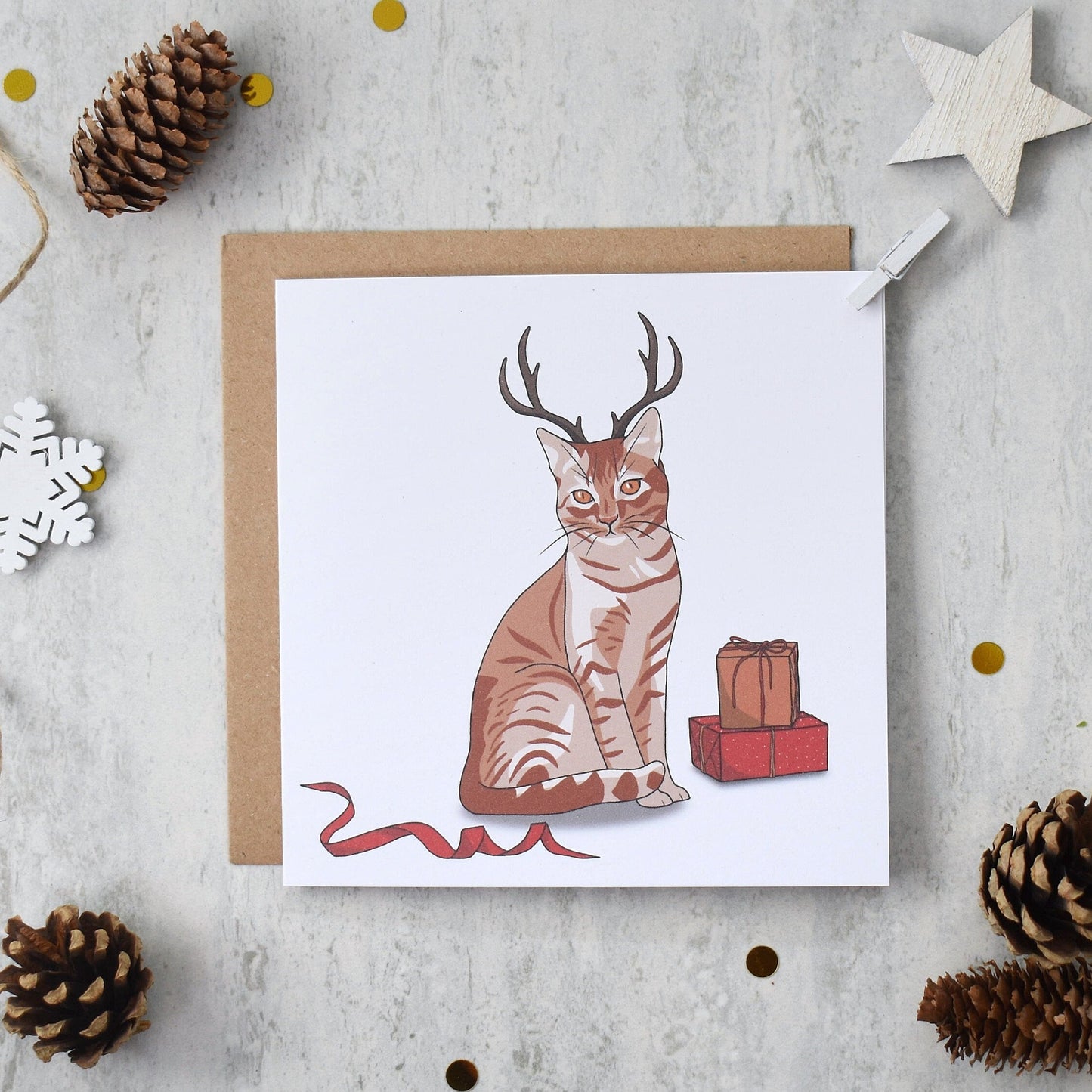 Greeting card with a cat wearing antlers on a textured surface with decorative elements.