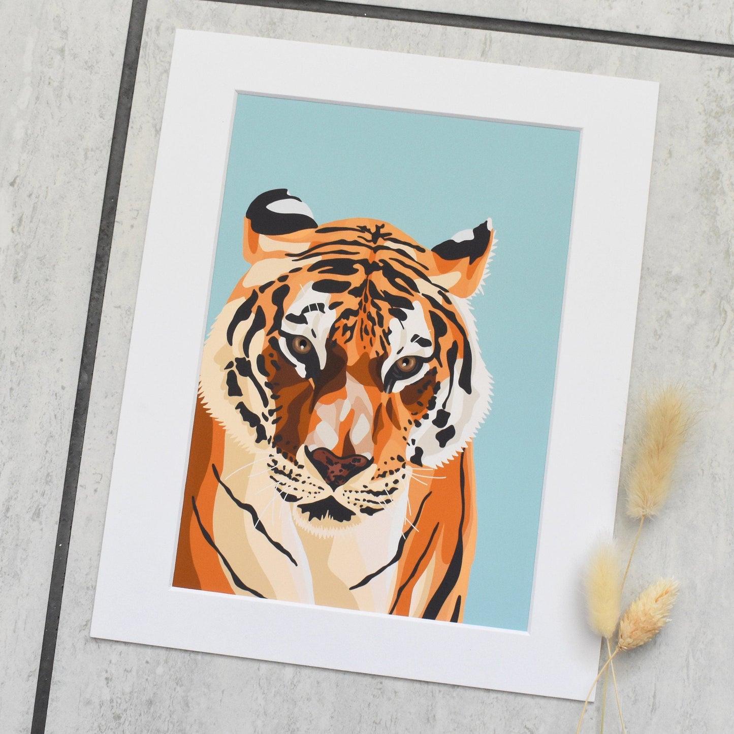Framed artwork of a tiger on a light blue background, placed on a textured surface.
