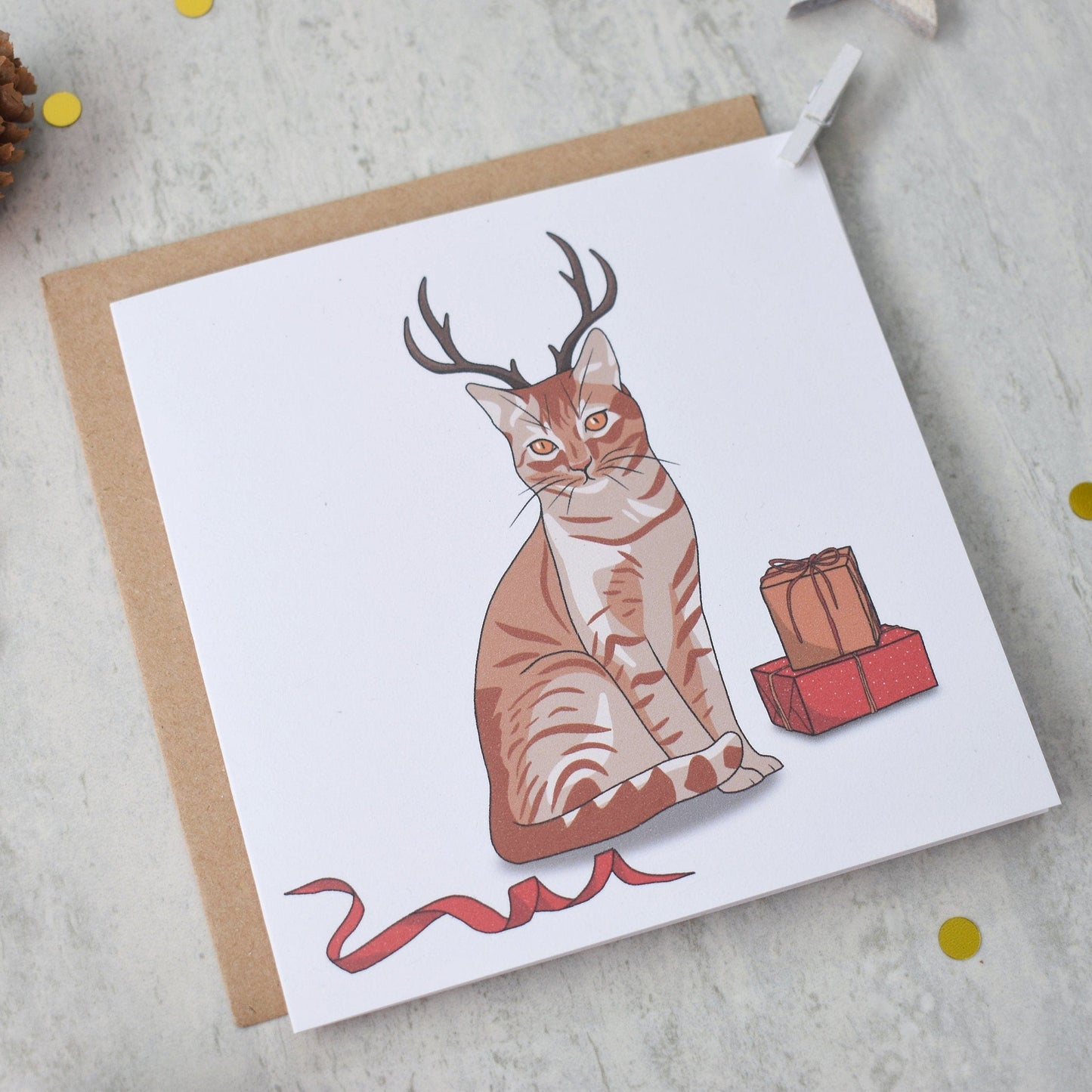 Greeting card with a cat wearing deer antlers on a textured surface with decorative elements.