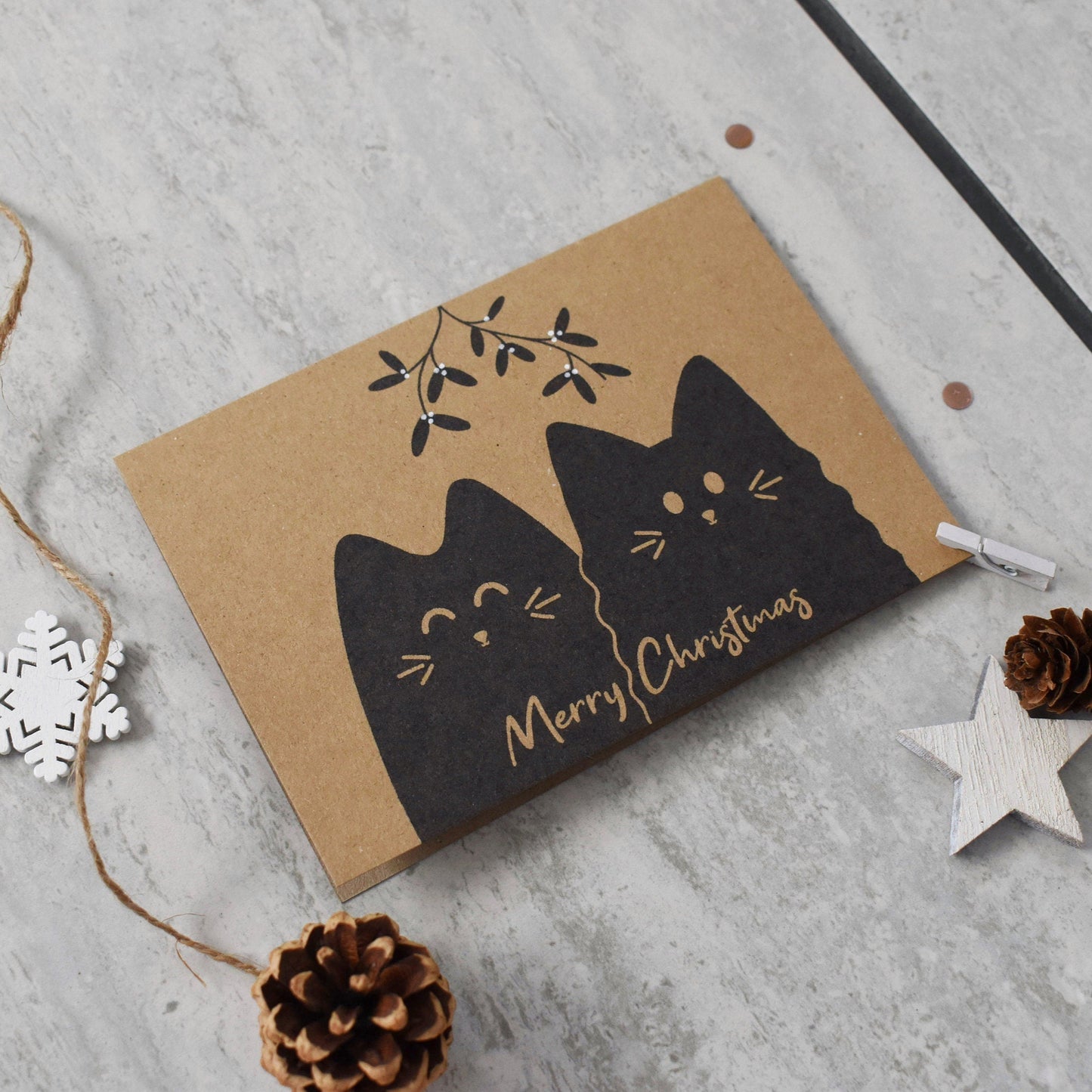 Card with black cat design and 'Merry Christmas' text on a gray surface with decorative elements.