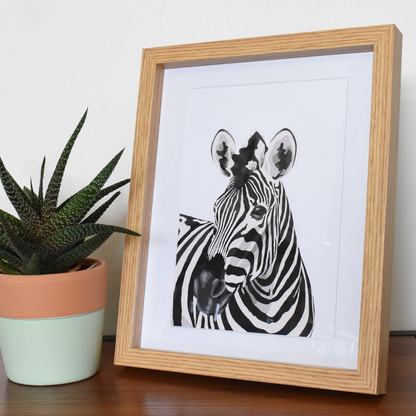 Framed black and white zebra print next to a potted plant on a wooden surface.