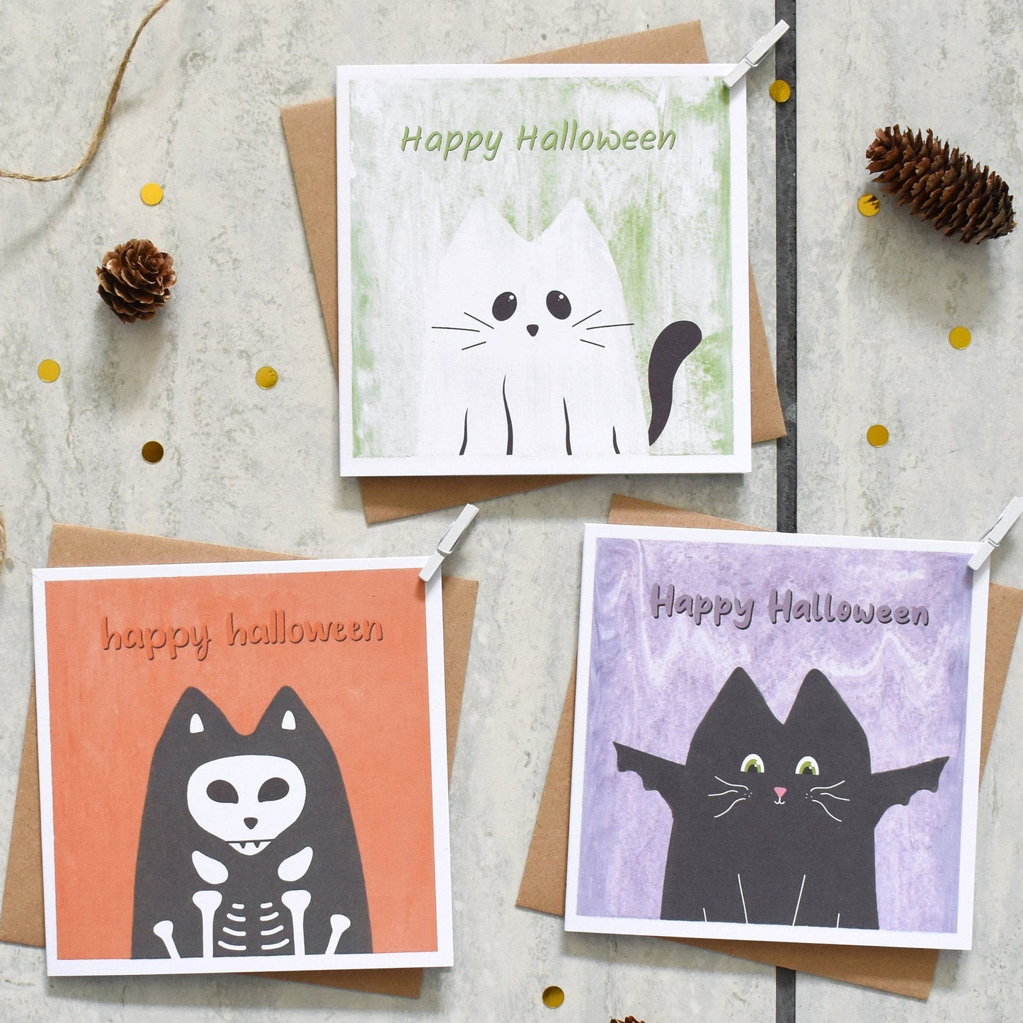 Three Halloween-themed greeting cards with cat illustrations on a textured surface.