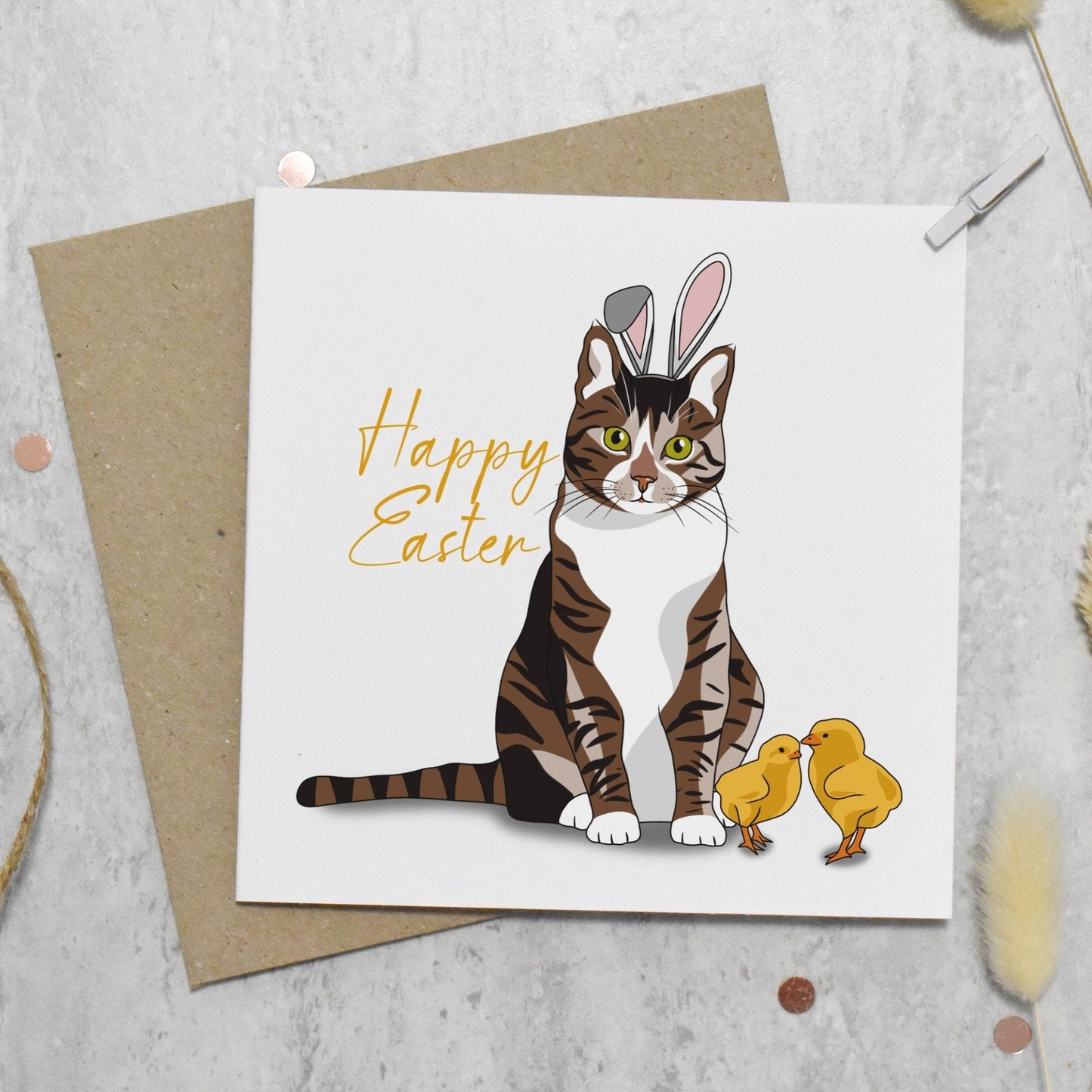 Easter card with a cat wearing bunny ears and two chicks on a gray surface.
