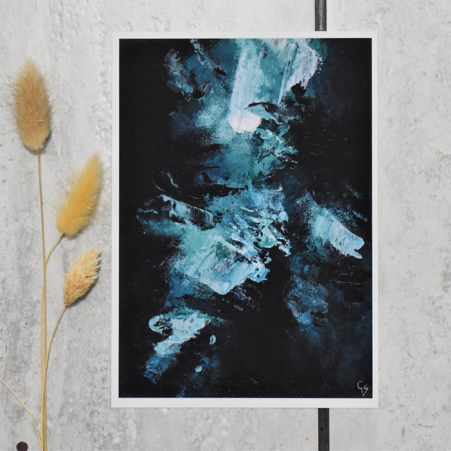 Abstract art print on a textured wall with dried plants.