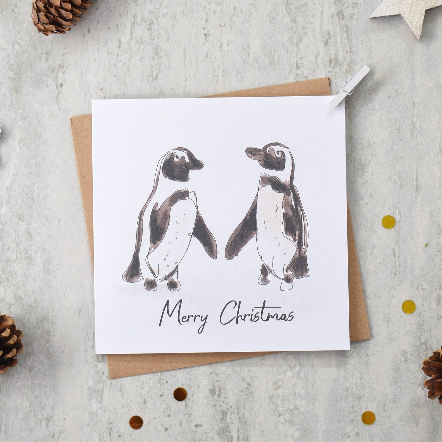 Christmas card with penguin illustration on a gray surface with festive decorations.