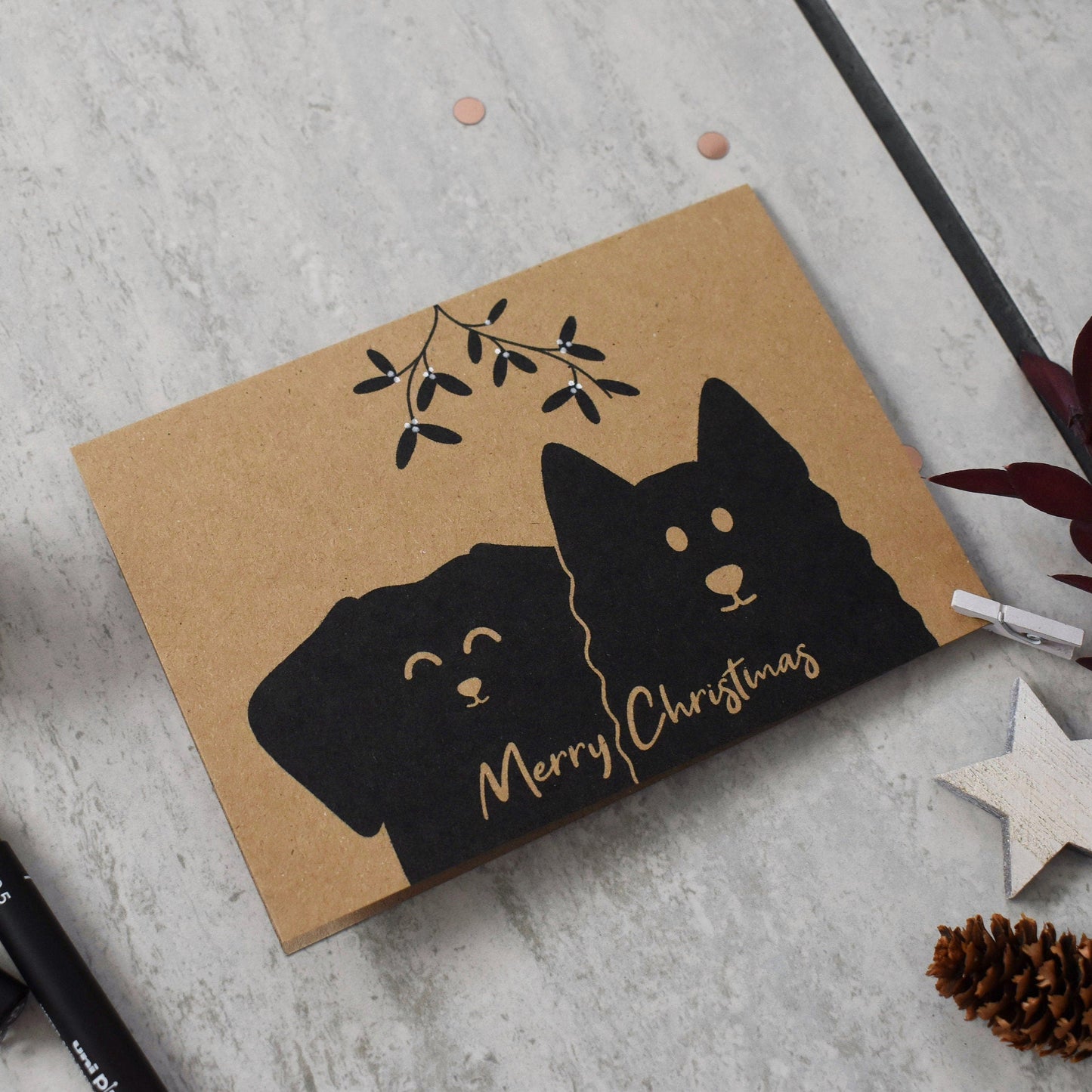 Card with black dog illustrations and 'Merry Christmas' text on a textured surface with decorative items.