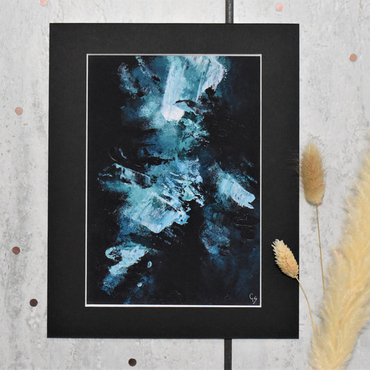 Abstract art print in a black frame on a textured wall with dried plants.