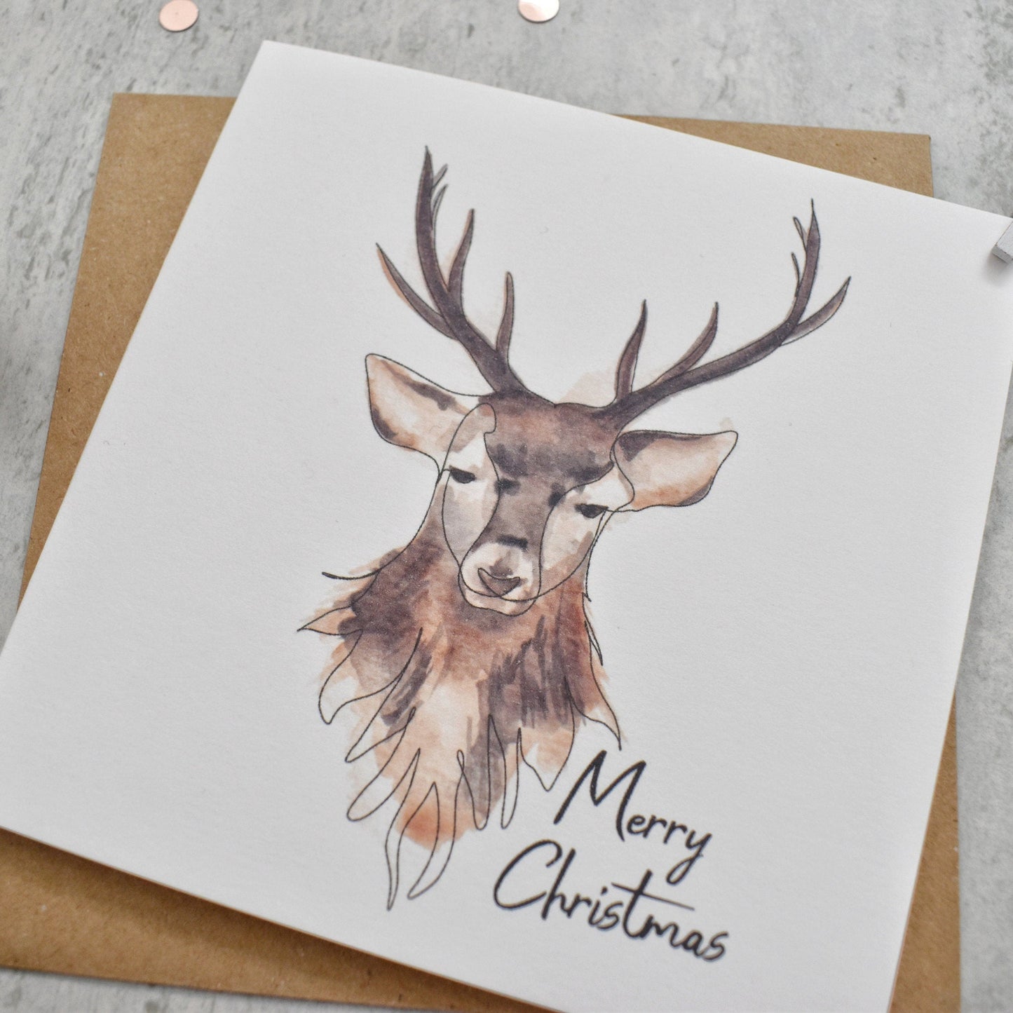 Christmas card with a deer illustration and 'Merry Christmas' text on a gray surface.
