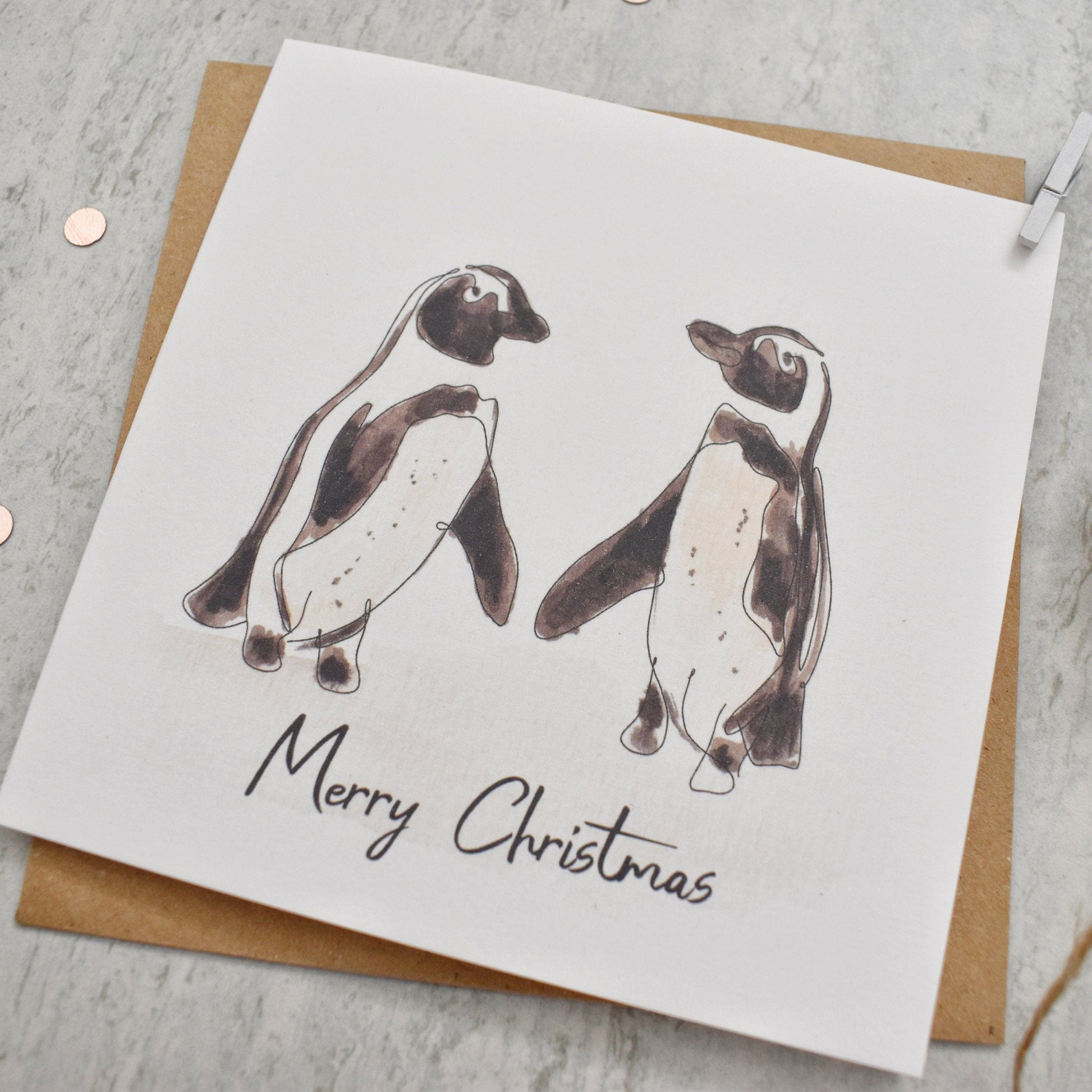 Christmas card with penguin illustration and 'Merry Christmas' text on a gray surface.