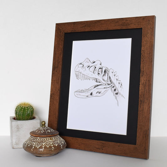 Framed black and white illustration of a dinosaur skeleton on a white surface with decorative items.