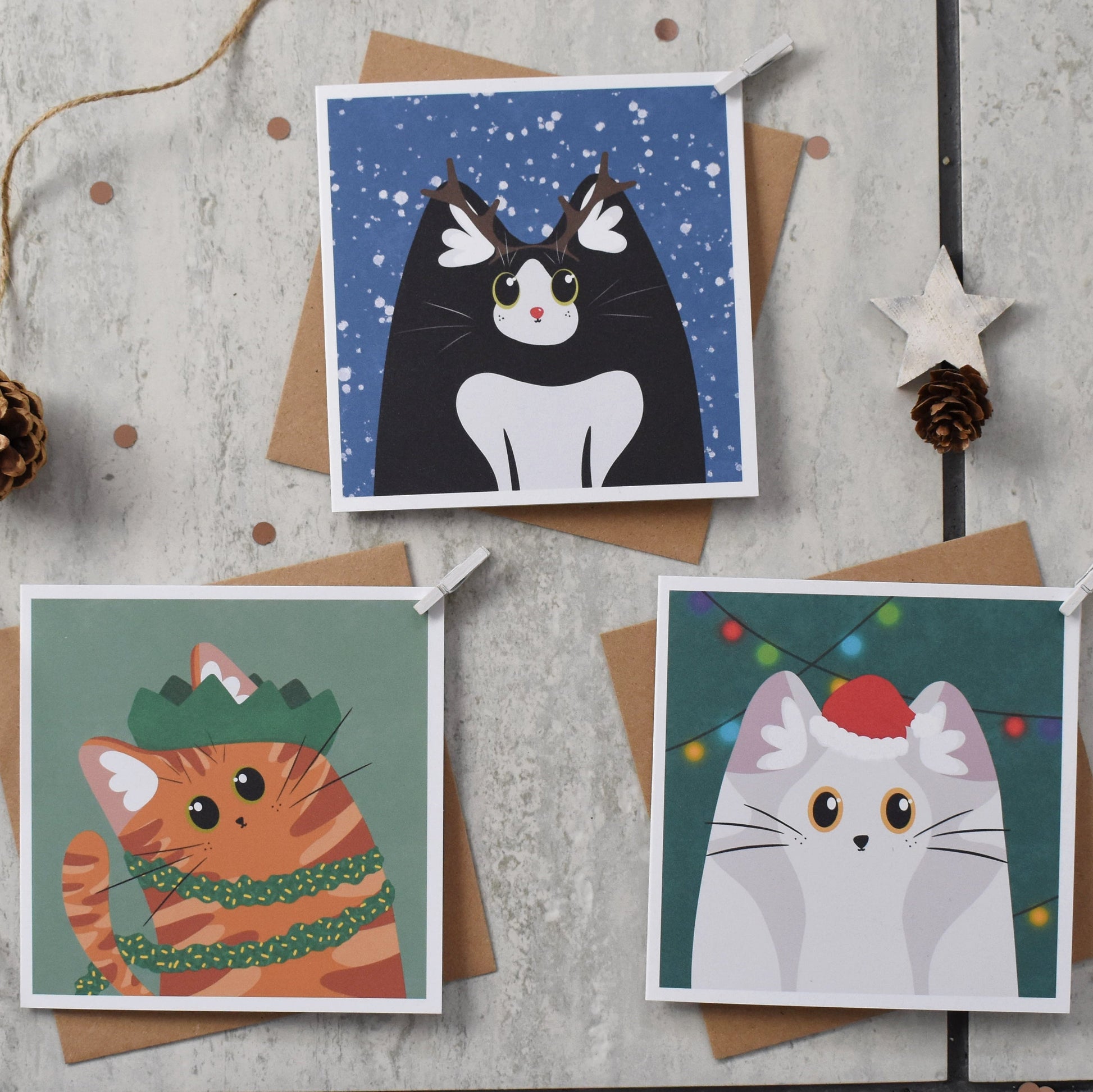Three Christmas-themed cat cards on a wooden surface with decorative elements.