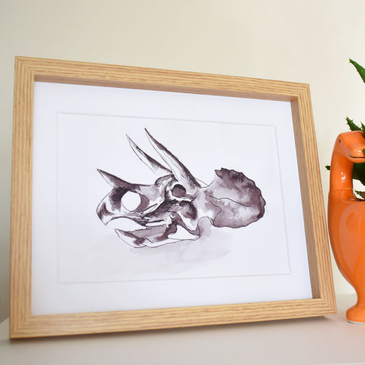 Framed artwork of a dinosaur skull next to an orange dinosaur-shaped planter with a plant.