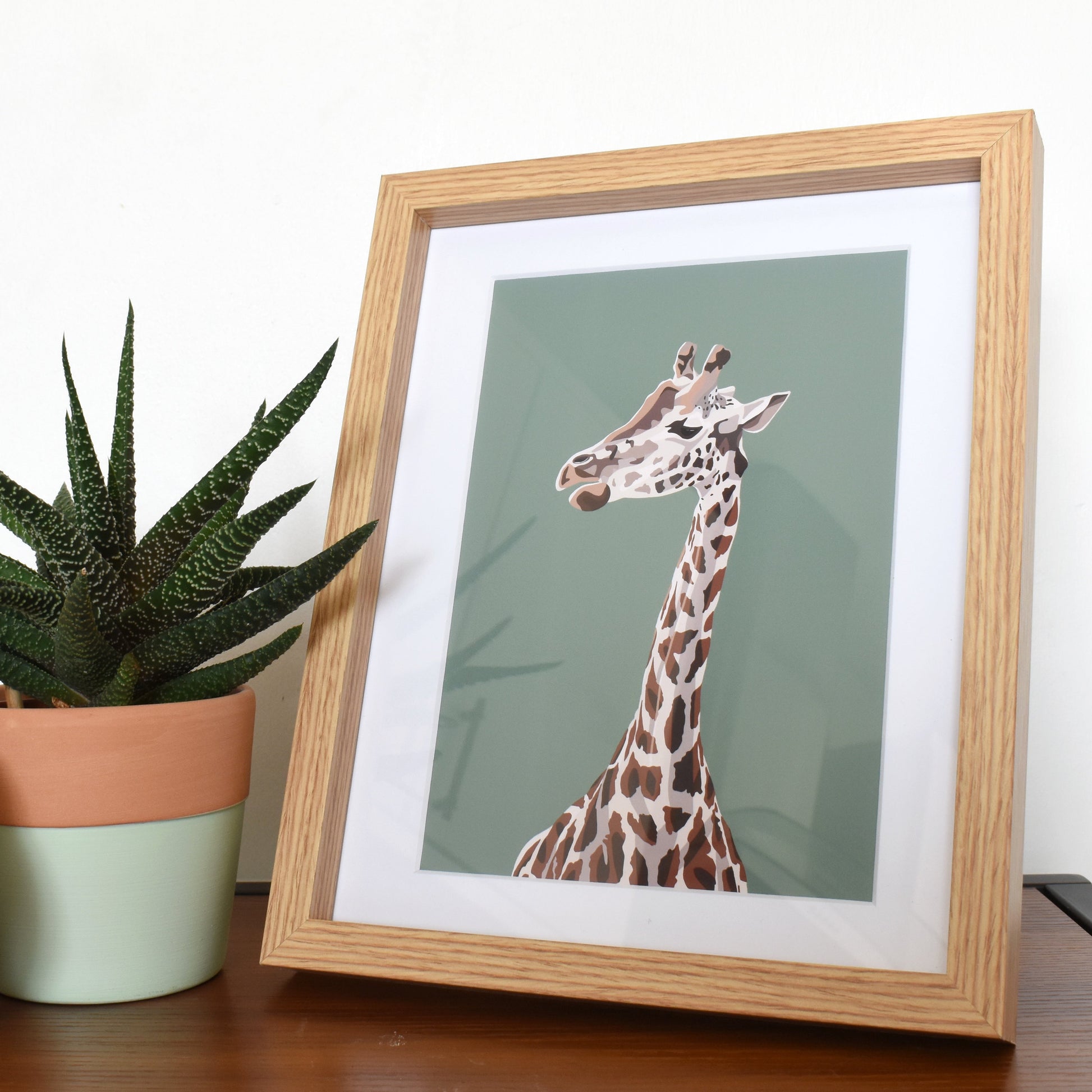 Framed picture of a giraffe on a table with potted plants
