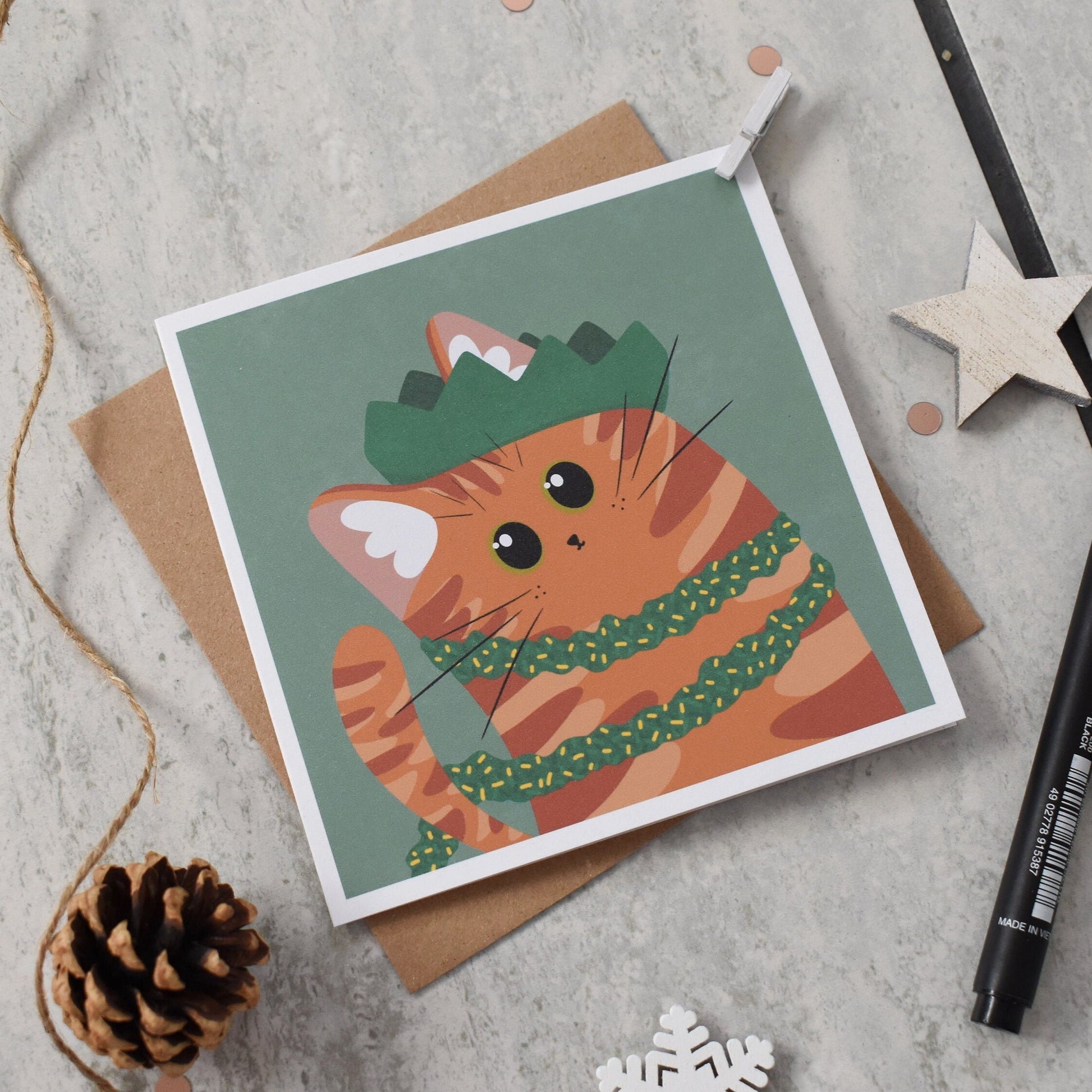 Greeting card with a cat illustration wearing a party hat and tinsel on a textured surface.