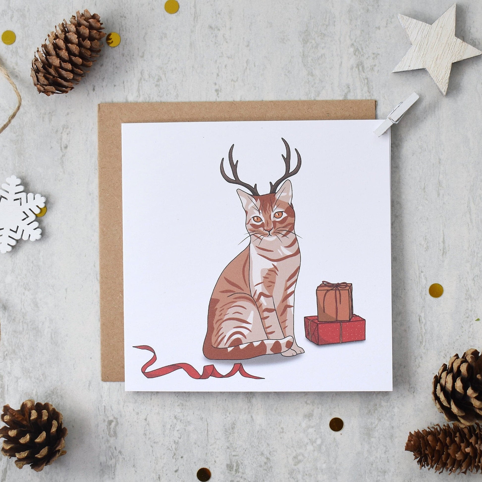 Greeting card with a cat wearing antlers on a textured surface with decorative elements.