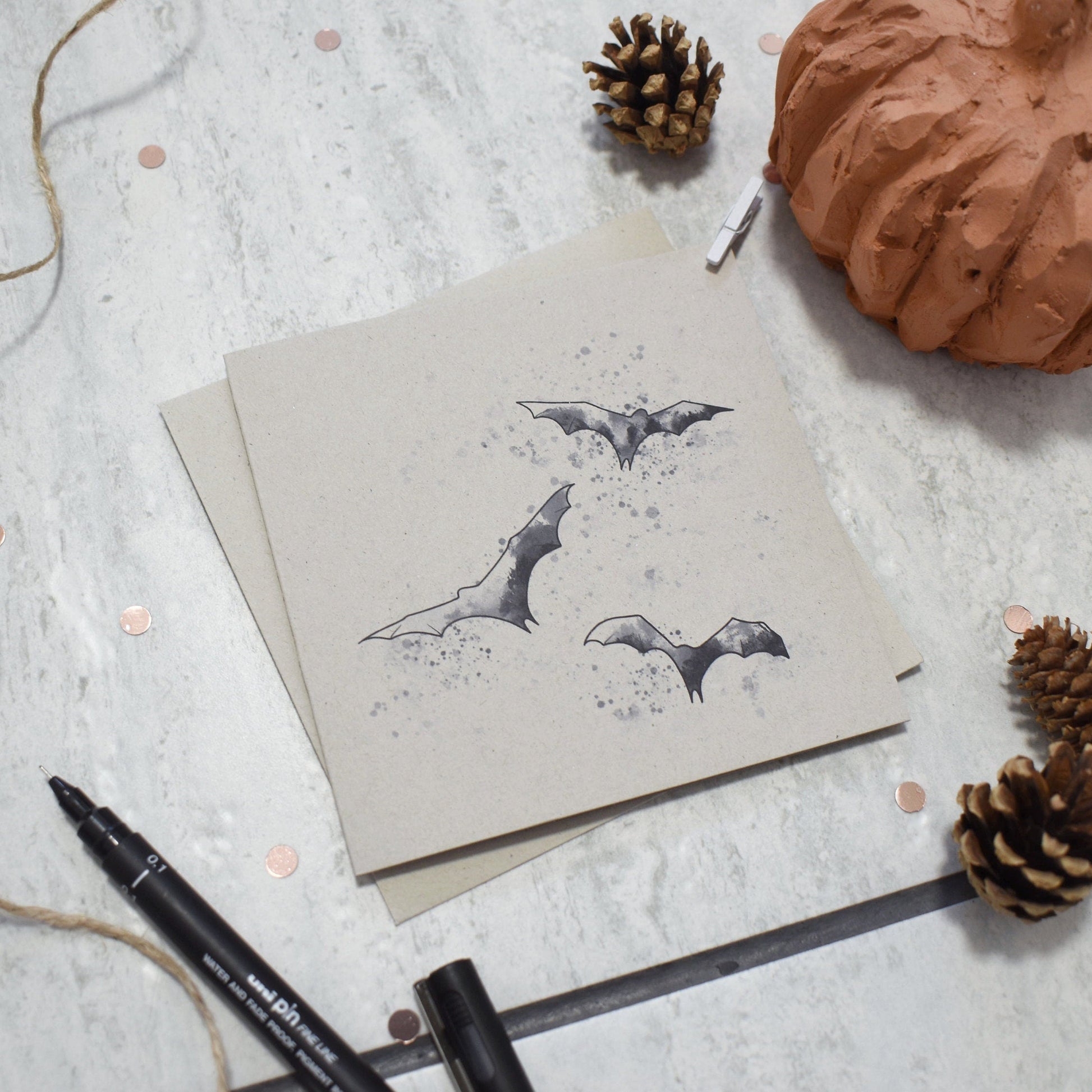 Card with bat illustrations on a textured surface with pumpkins and pinecones.
