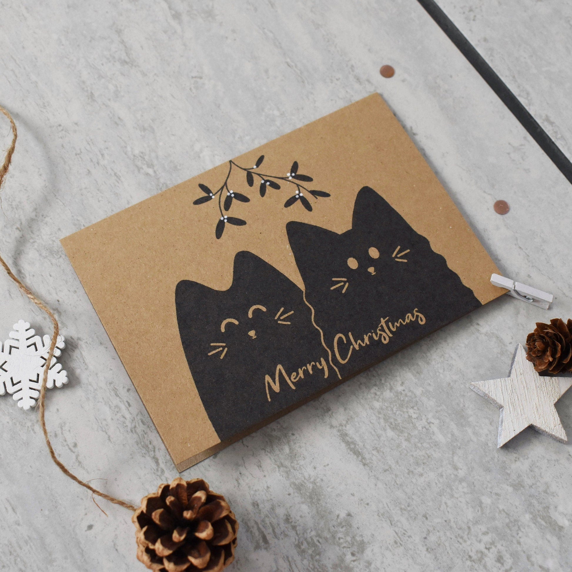 Card with black cat design and 'Merry Christmas' text on a gray surface with decorative elements.