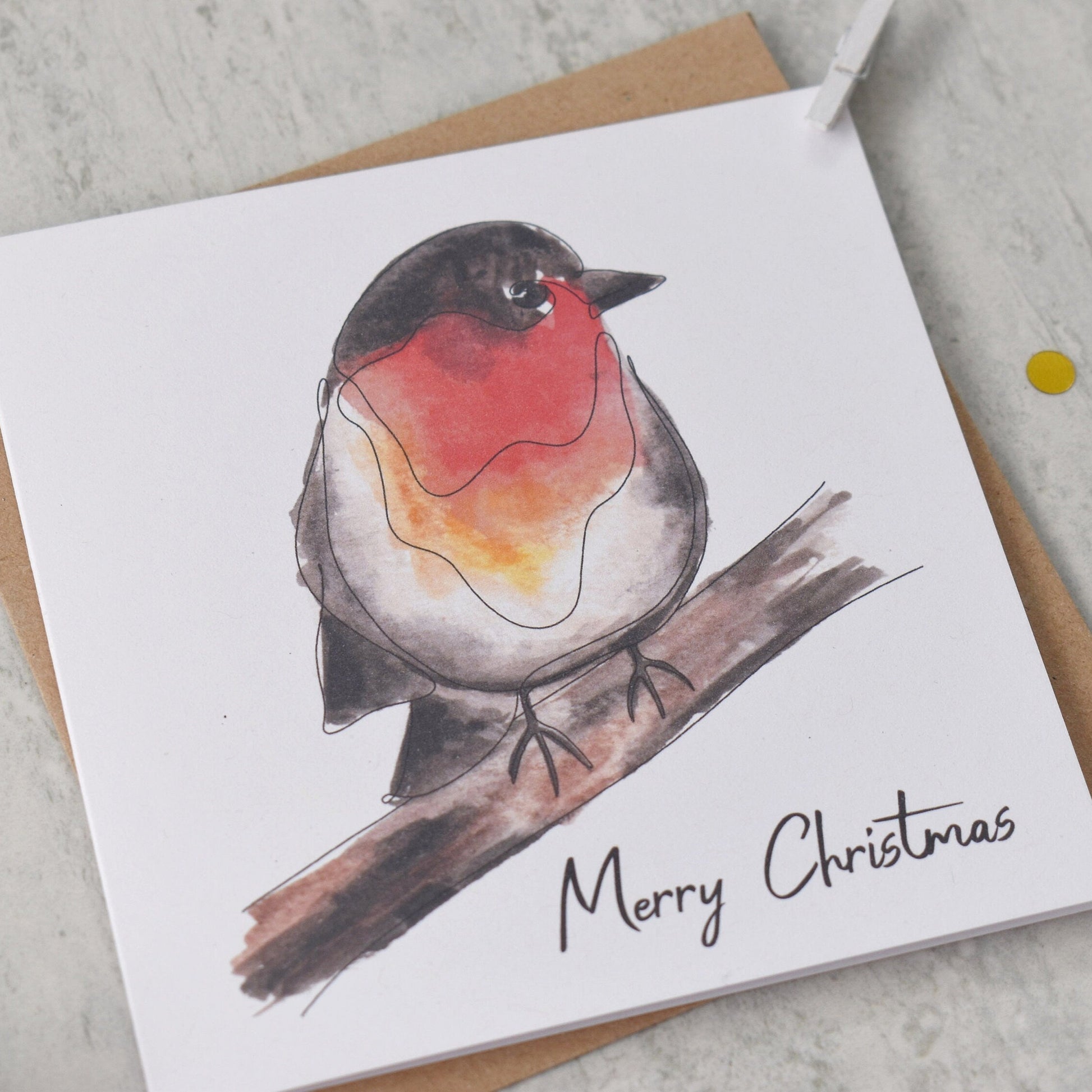 Christmas card with a robin illustration and 'Merry Christmas' text on a gray surface.